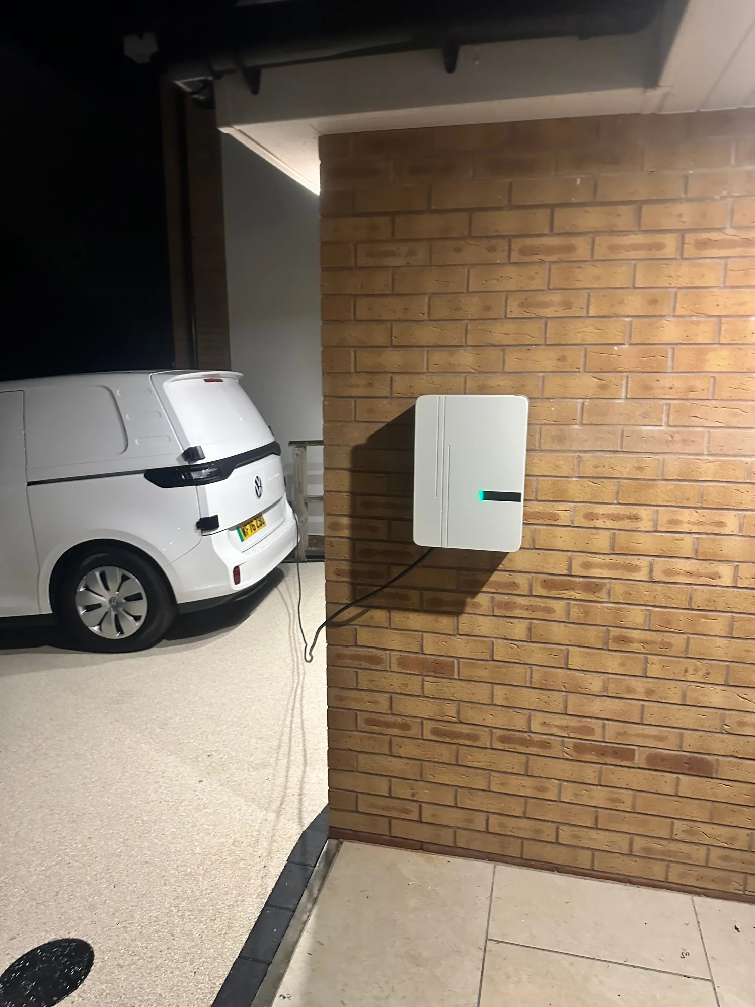 White wall-mounted home EV charger fitted on a brick wall