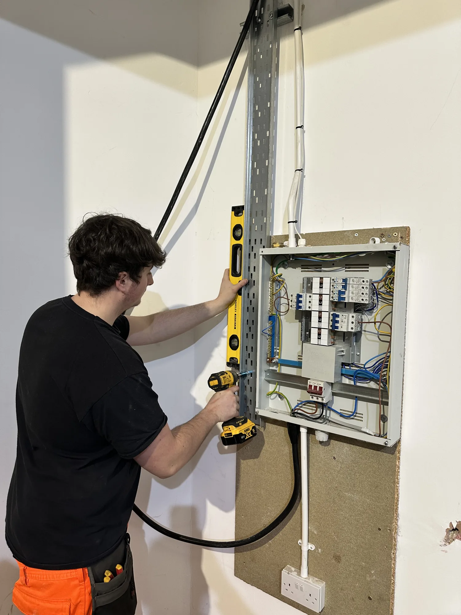 Electrician mounting a new consumer unit and trunking on a wall